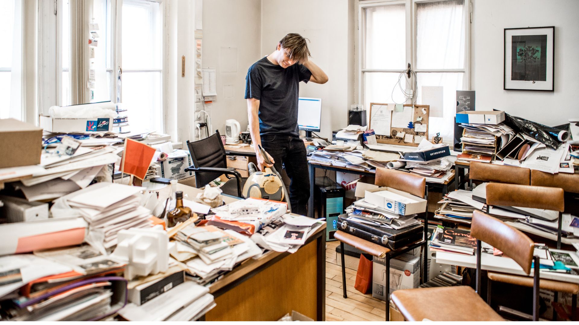 Young man in messy office with piles of paper everywhere